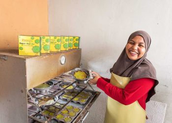 Sri Hidayani yang akrab disapa Mak Zai. Dengan cekatan, tangannya menuangkan adonan bolu berwarna hijau cerah ke dalam loyang, melanjutkan warisan keluarga yang telah lama terjaga.